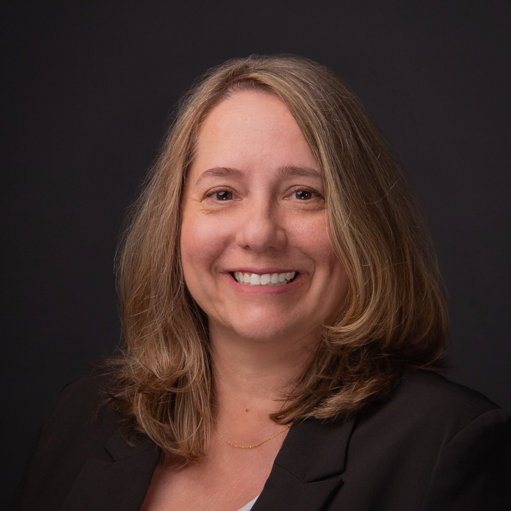 Mary Pavey is wearing a black blazer and has light skin, shoulder length light brown hair, brown eyes and is fair skinned.