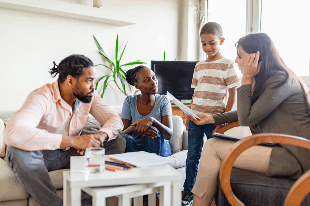 A family made up of Dad, Mom and a young son sit in the office of a doctor as she reads from a piece of paper. The dad and mom are sitting on a couch while the son is standing beside the doctor.