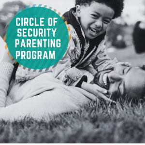 Circle of Security Parenting Program. An image of a young boy playing with his Dad on the grass. They are both laughing and rolling around.